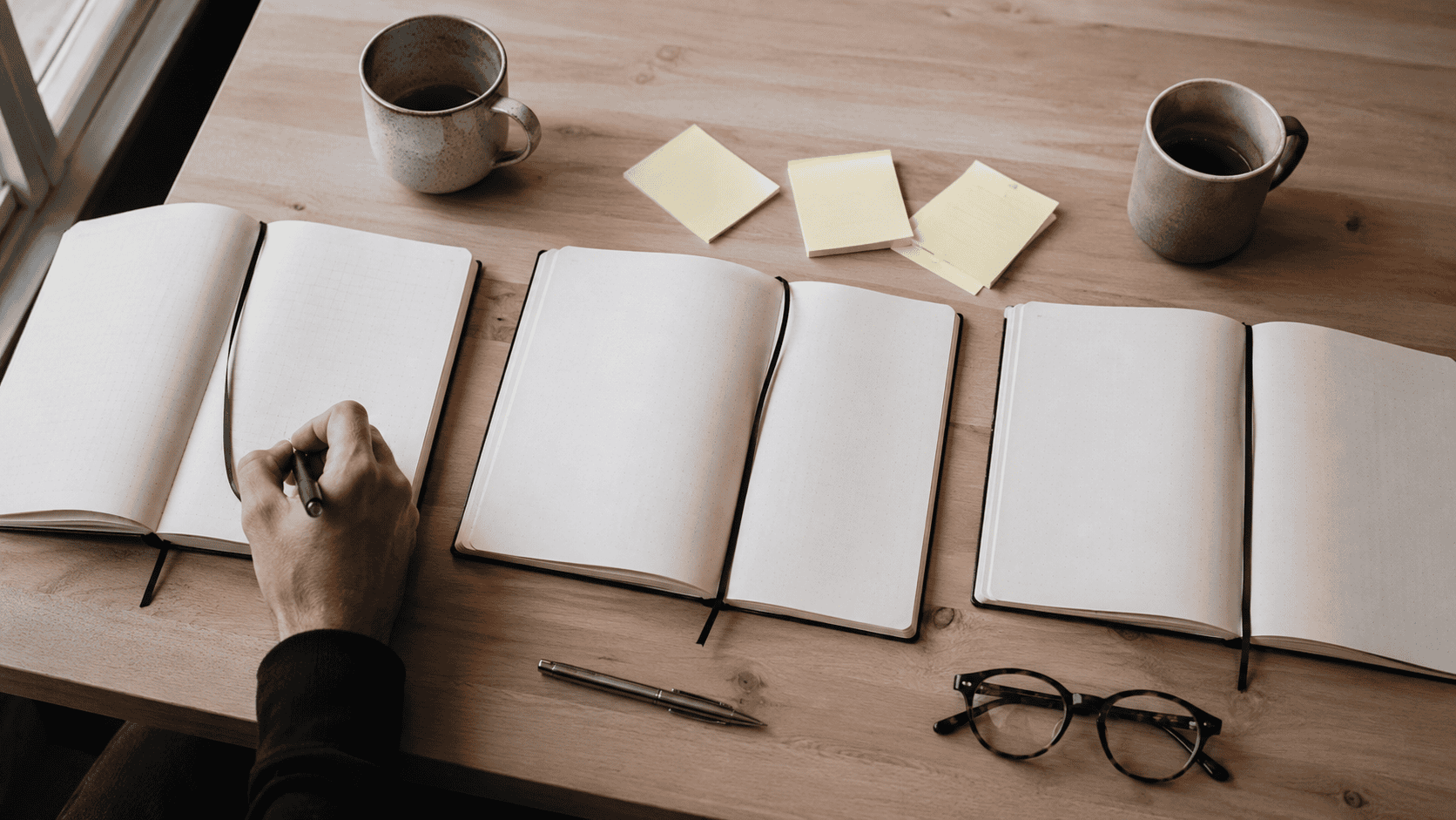 Tre åbne notesbøger med post-its og kaffekopper på et bord – arbejdsfordeling i bestyrelsen